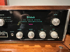 McIntosh C 26 solid state stereo preamplifier with a black front panel, silver control knobs, and a brown wood-grain cabinet, shown on a wooden surface.