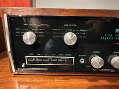 A vintage C-26 stereo receiver left front panel with a black faceplate, silver control knobs, and a brown wood-grain cabinet, shown on a wooden surface.