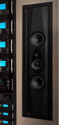 Row of audio equipment with digital displays on a wall next to a large in-wall speaker.