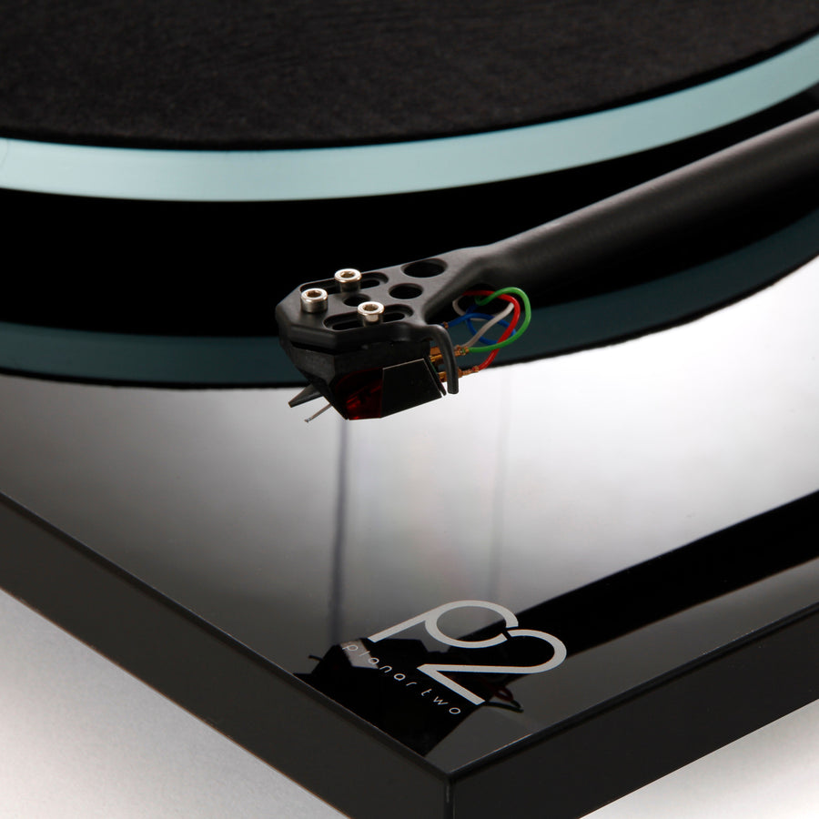 Close-up of a turntable cartridge on a black turntable with 'Rega' branding.