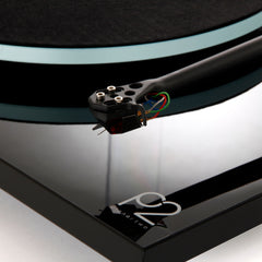 Close-up of a turntable cartridge on a black turntable with 'Rega' branding.