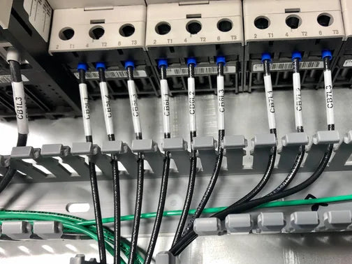 Cable management system with labeled cables and a green label on a metallic surface.